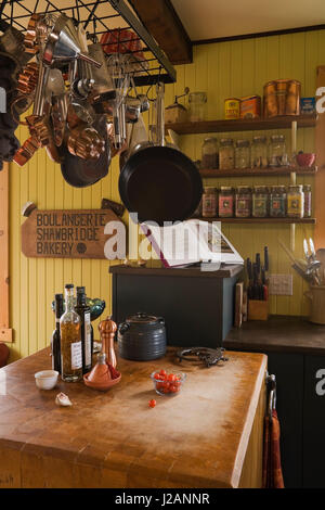 Hanging pots and pans over a wooden countertop table in the kitchen inside a country cottage style residential home Stock Photo
