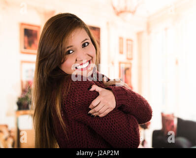 Pretty young brunette woman wearing red sweater, rubbing shoulders as being cold Stock Photo