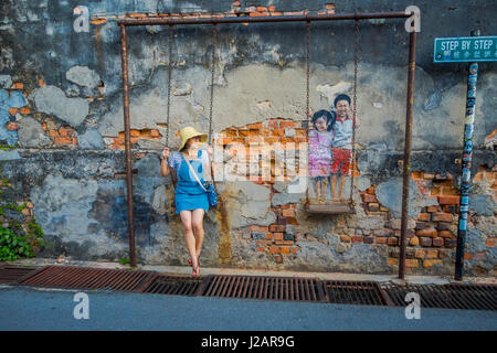 George Town, Malaysia - March 10, 2017: Unknown woman tourist and the Children on the Swing mural street art. Stock Photo