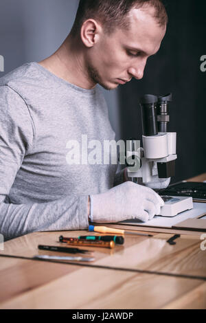 Young male technician examining circuit board with microscope at electronics store Stock Photo