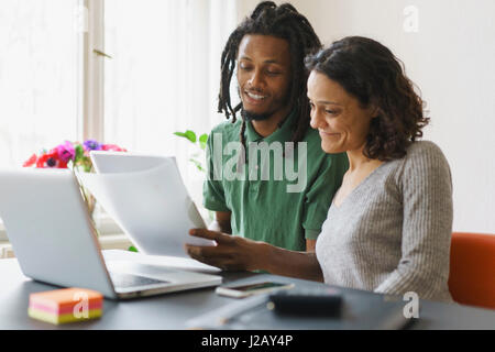 Couple reading documents while sitting with laptop at table Stock Photo