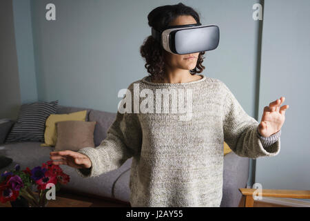 Woman using virtual reality headset while standing in living room Stock Photo