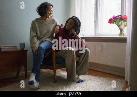 Smiling couple looking at each other while sitting on armchair at home Stock Photo