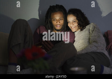 Smiling multi-ethnic couple using digital tablet in dark living room Stock Photo