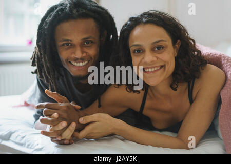 Portrait of happy couple holding hands while lying in bed at home Stock Photo