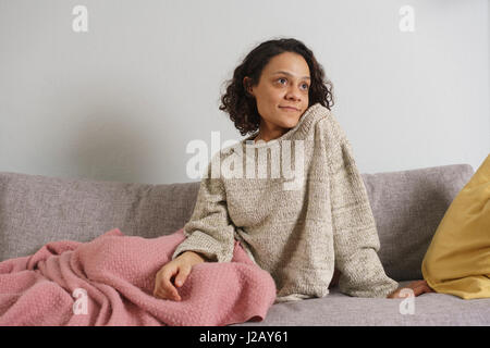 Thoughtful woman looking away while sitting on sofa at home Stock Photo