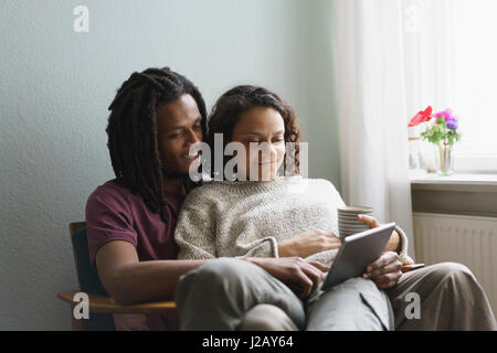Young multi-ethnic couple using digital tablet while sitting on armchair at home Stock Photo