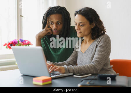 Couple using laptop at table in house Stock Photo
