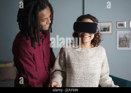 Happy man looking at woman using virtual reality headset in living room Stock Photo