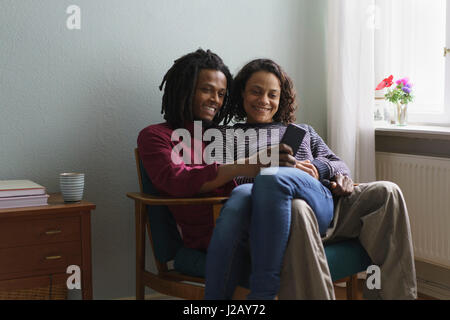 Smiling multi-ethnic couple using smart phone while sitting on armchair at home Stock Photo