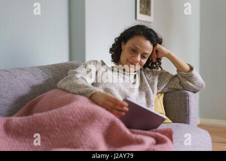 Smiling woman using digital tablet while relaxing on sofa at home Stock Photo