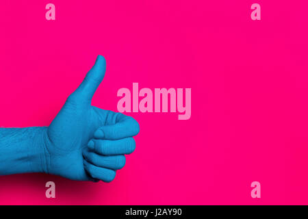 Close-up of blue painted hand showing thumb up against pink background Stock Photo