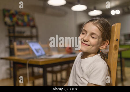 Portrait of smiling girl sitting with eyes closed on wooden chair at home Stock Photo