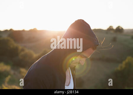 Side view of man wearing hooded jacket on field during sunny day Stock Photo