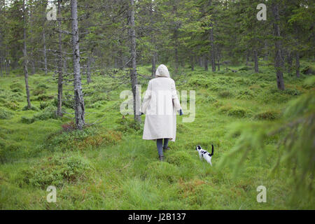 Rear view of woman wearing long coat while walking with cat on grassy field Stock Photo