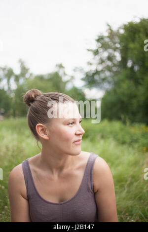 Thoughtful mid adult woman looking away while sitting on field Stock Photo