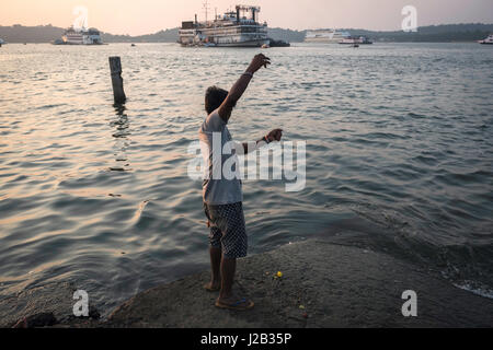 A fisherman tries to catch a fish in front of one of the boats used as a casino in Panjim Stock Photo