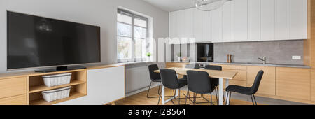 Panorama of modern home interior with open kitchen, dining space and big tv screen Stock Photo