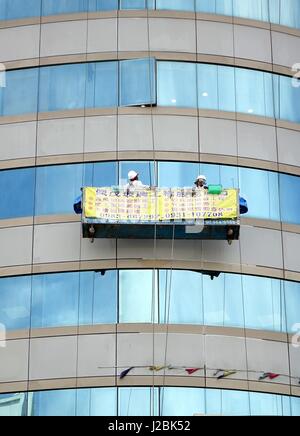 KAOHSIUNG, TAIWAN -- JUNE 27, 2014: Two unidentified workers perform the dangerous task of washing the windows of an office tower Stock Photo