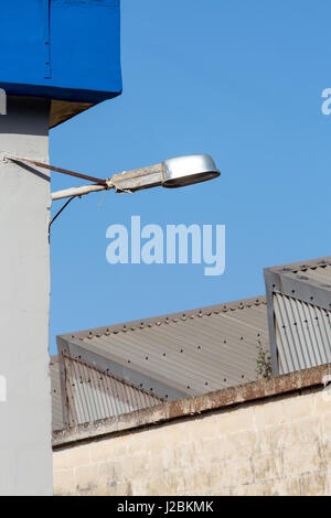 Streetlight on the outside of a factory with corrugated iron roofing and blue sky in the background. Industrial estate / area, Marsa, Malta. Stock Photo