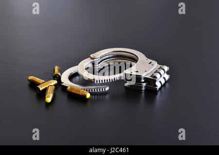 Police handcuffs and pistol bullets on dark table Stock Photo