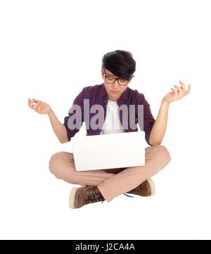 A young Asian student sitting on the floor with his laptop and is perplexed what he sees in the screen, isolated for white background. Stock Photo