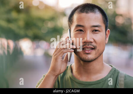 Handsome Asian man talking on his cellphone outdoors Stock Photo