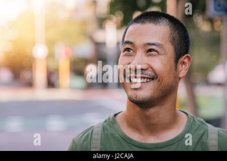 Handsome young Asian man standing on a city street smiling Stock Photo