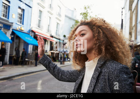 Stylish Young Woman Hailing Taxi On Busy City Street Stock Photo