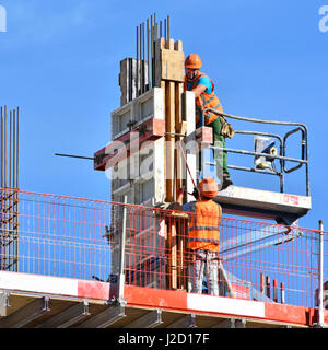 Health & safety uk  building construction site worker fixing column formwork workers wearing hard hats & high visibility jacket on high rise building Stock Photo