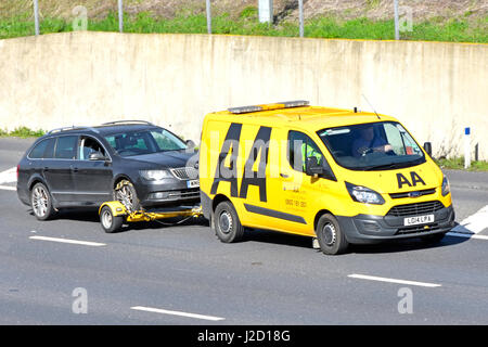 Broken down Ford car being towed along M25 motorway by yellow AA branded business Volkswagen breakdown van with high vis driver & passenger England UK Stock Photo