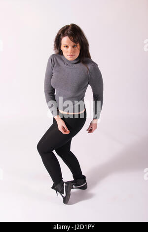 Beautiful brunette girl in the studio wearing black leggings and grey jumper Stock Photo