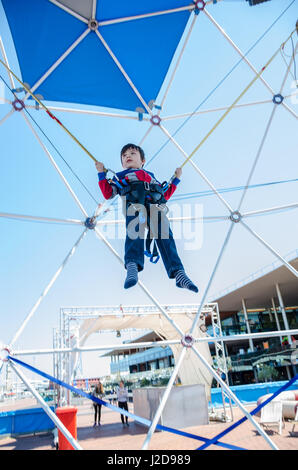 A young boy bounces on a trampoline while attached to bungie ropes to allow him to bounce higher. Stock Photo