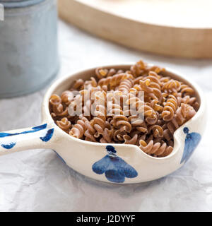 square image of pasta made from brown rice gluten free, uncooked in a small dish shot in window light with an out of focus background to add text or c Stock Photo
