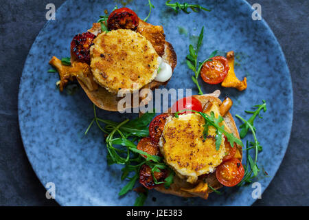 Baked goat cheese on sourdough bread with chanterelle mushrooms and cherry tomatoes Stock Photo