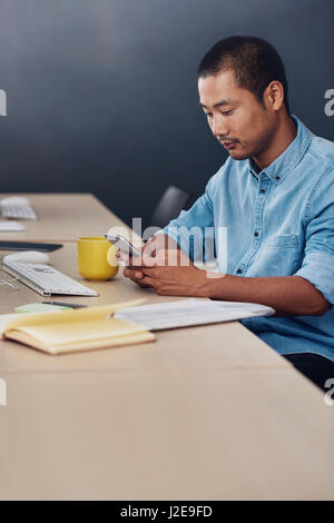 Focused Asian designer sitting at his desk using a cellphone Stock Photo