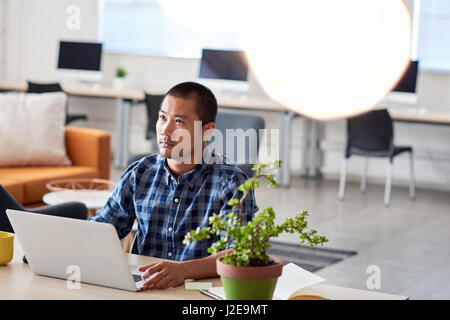 Focused Asian designer deep in thought working on a laptop Stock Photo