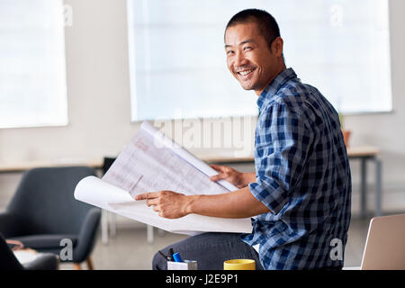 Smiling Asian architect reading blueprints in an office Stock Photo