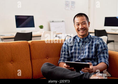 Smiling Asian designer using on a digital tablet at work Stock Photo