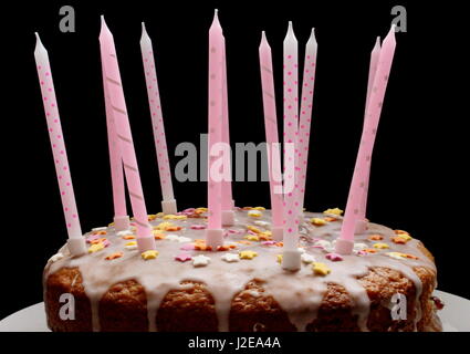 A celebration cake, with icing, hundreds and thousands decoration, and pink candles, on a black background Stock Photo