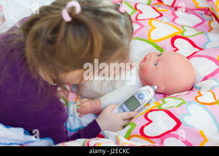 Little girl playing doctor with a doll, measuring temperature with electronic themometer and taking care of a doll, concept maternity, lifestyle and c Stock Photo