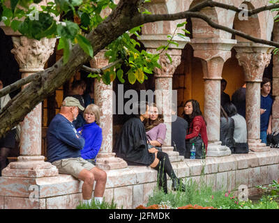 Perched on a wall with columns, multiracial visitors of different ages enjoy the Cuxa Cloister garden at The Cloisters Museum, a restored medieval monastery in Ft. Tryon Park, New York City. Stock Photo