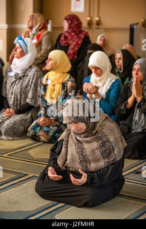 Wearing a hijabs or head scarves in a separate area, Muslim women kneel in Abrahamic prayer while listening to the sermon or Khutbah during religious services at an Anaheim, CA, mosque. Note traditional Middle Eastern clothing. Stock Photo