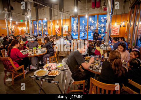 Tables at a Korean barbecue restaurant in Buena Park, CA, include integral stoves for cooking meat and vents to remove smoke. Note fresh ingredients on tray in center. Stock Photo