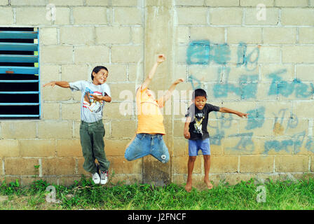 Belize, El Progreso, children jumping in the air in front of cement wall at school Stock Photo