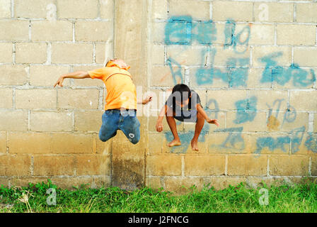 Belize, El Progreso, children jumping in the air in front of cement wall at school Stock Photo