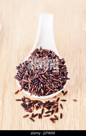 Thai black jasmine rice or Rice berry in white spoon in wooden background. Stock Photo