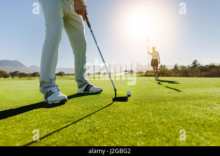 Low angle view of golfer on putting green about to take the shot. Male golf player putting on green with second female player in the background holdin Stock Photo
