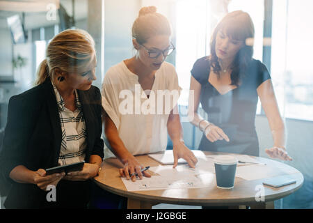 Business people standing at the table and discussing new projects. Female executives looking at papers on table and brainstorming. Stock Photo