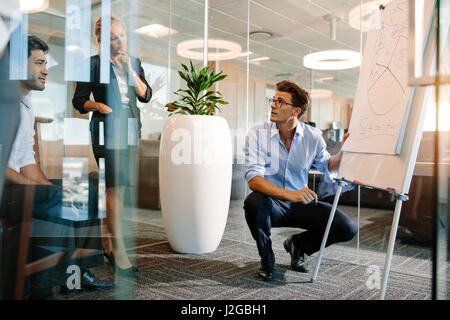 Mature man making a presentation on a flip-chart. Businessman explaining pie chart to colleagues during a meeting.